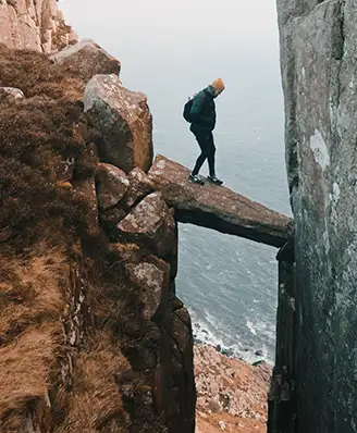 Person walking along a rock spanning two cliffs