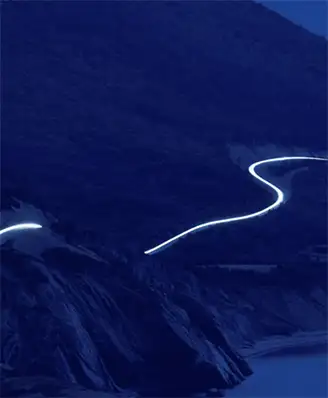 Mountain at night with a time lapse streak of headlights along the road.