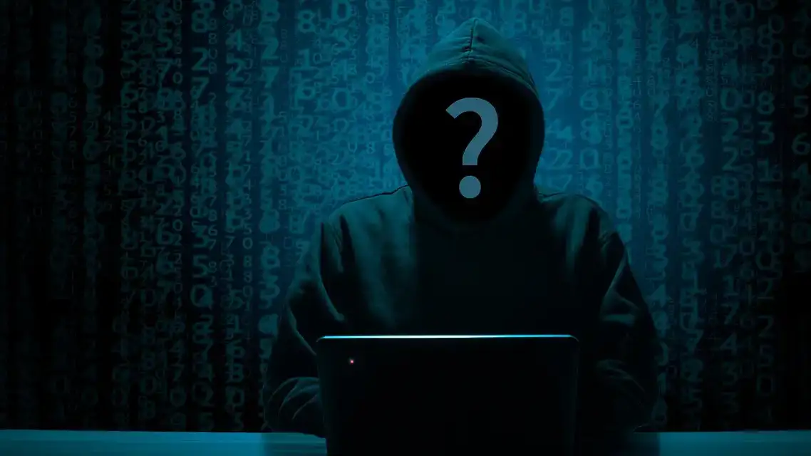 Shadowy figure in a hoodie accessing data on a laptop.